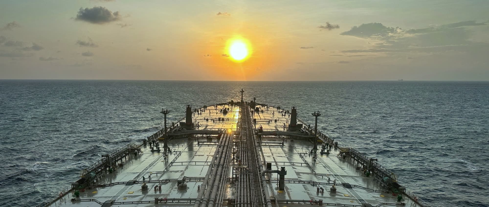 View along a tanker's deck and cargo lines towards the bow, sailing into the sunset